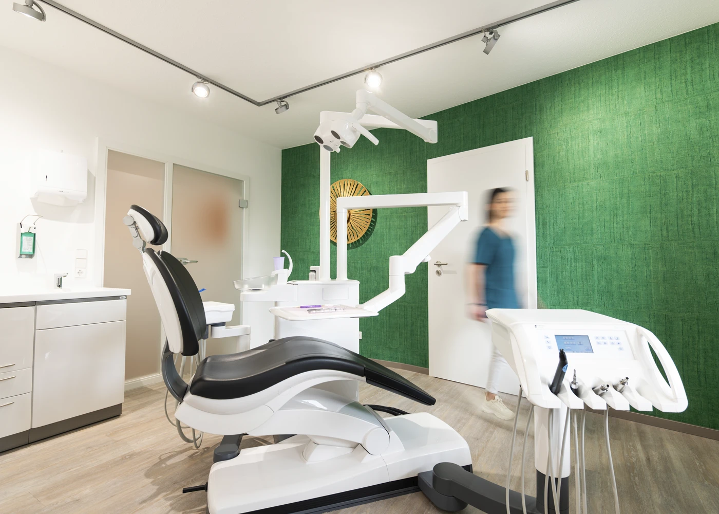 Moderne Zahnarztpraxis mit Behandlungsstuhl, grüner Wand und Gerät.